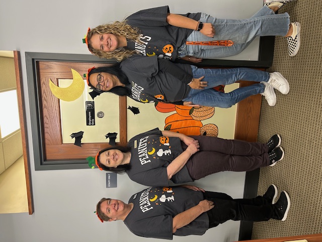 The library administration department all in Peanuts Halloween t-shirts featuring Snoopy. From left to right, library director Sheila, library operations manager Dina, public relations specialist Stephanie, and senior library assistant Jace.
