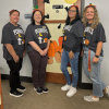 The library administration department all in Peanuts Halloween t-shirts featuring Snoopy. From left to right, library director Sheila, library operations manager Dina, public relations specialist Stephanie, and senior library assistant Jace.