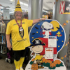 Barb, dressed up as a yellow crayon, stands beside a cardboard display featuring Peanuts characters Charile Brown, dressed as a pirate, and Snoopy, dressed as a vampire
