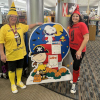 Barb, dressed up as a yellow crayon, and Rabecca, dressed up as a red crayon, stand beside a cardboard display featuring Peanuts characters Charile Brown, dressed as a pirate, and Snoopy, dressed as a vampire