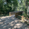 A dirt path lined with trees and shrubs leads to a wooden bridge